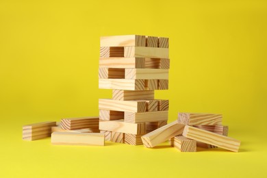 Jenga tower and wooden blocks on yellow background