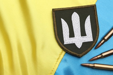 Bullets and military patch on Ukrainian flag, flat lay. Space for text