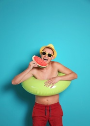 Shirtless man with inflatable ring eating watermelon on color background