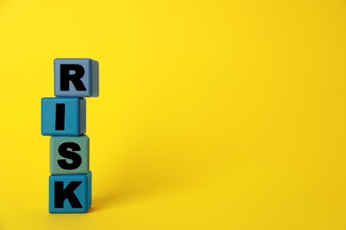 Word Risk made of colorful cubes on yellow background, space for text