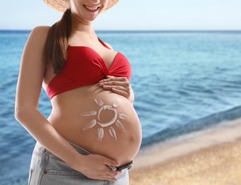 Young pregnant woman with sun protection cream on beach, closeup