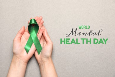 World Mental Health Day. Woman holding green ribbon on light grey background, top view