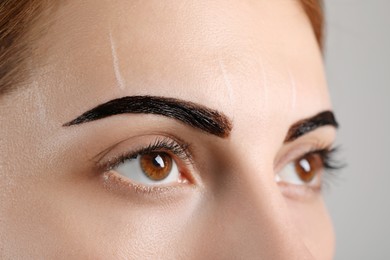 Woman during eyebrow tinting procedure on grey background, closeup