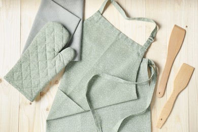 Kitchen napkin, apron, glove and spatulas on wooden table, flat lay