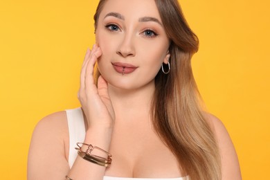 Photo of Young woman with lip and ear piercings on yellow background