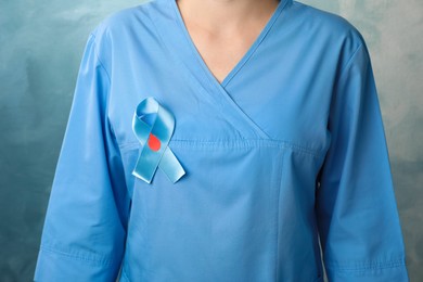Photo of Doctor with light blue ribbon and paper blood drop on color background, closeup. World Diabetes Day