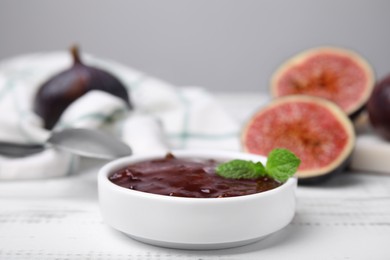 Photo of Tasty sweet fig jam and fruits on white wooden table, closeup