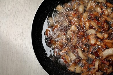 Photo of Tasty cooked cracklings in frying pan on light wooden table, top view. Pork lard