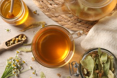 Freshly brewed tea, honey and dried herbs on white wooden table, flat lay