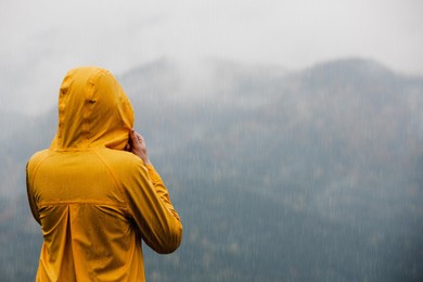 Woman in raincoat enjoying mountain landscape under rain, back view