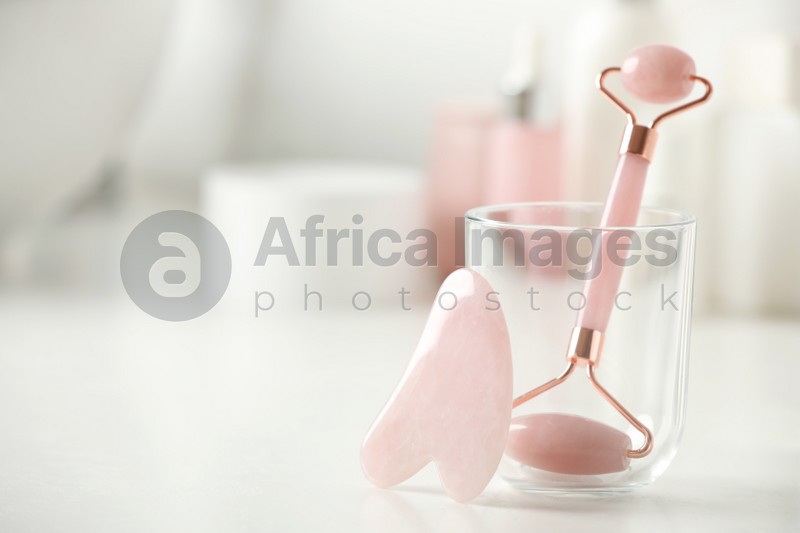 Natural face roller and gua sha tool on white table against blurred background, closeup. Space for text