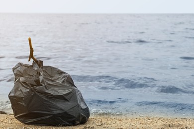 Trash bag full of garbage on beach. Space for text