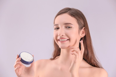 Teenage girl with acne problem using cream against grey background