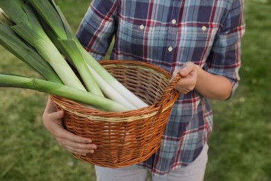 Woman holding wicker basket with fresh raw leeks outdoors, closeup