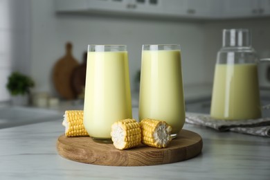 Photo of Tasty fresh corn milk in glasses and cobs on white table indoors
