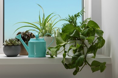 Photo of Different beautiful houseplants and light blue metal watering can on window sill indoors