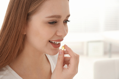 Young woman taking vitamin capsule on light background