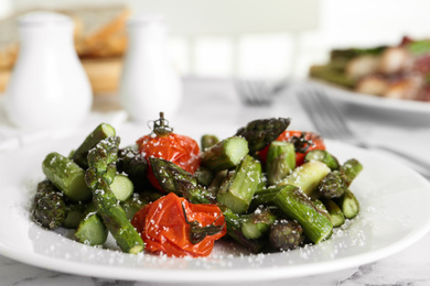 Oven baked asparagus with cherry tomatoes on white plate, closeup