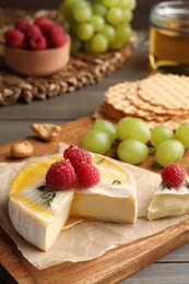Brie cheese served with berries and honey on wooden table, closeup