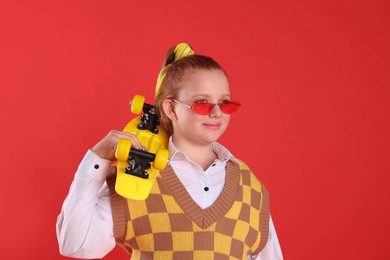 Cute indie girl with sunglasses and penny board on red background