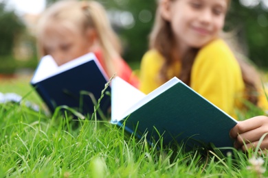 Little children reading books on green grass, closeup