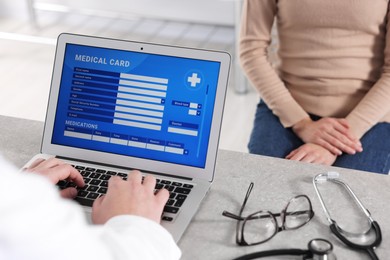 Photo of Doctor using laptop to fill out patient's medical card at table in clinic, closeup