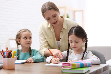 Mother helping her daughters with homework at table indoors