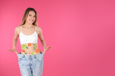 Slim woman in oversized jeans and images of vegetables on her belly against pink background. Healthy eating