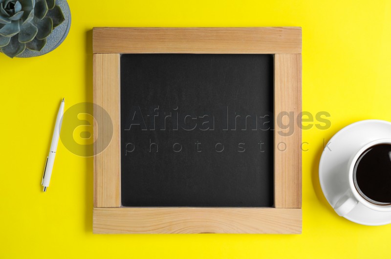 Clean small chalkboard, coffee, pen and plant on yellow background, flat lay
