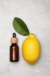 Bottle of essential oil with lemon and leaf on grey table, flat lay