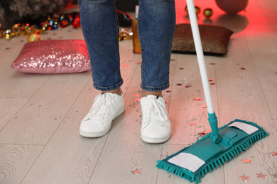 Man with mop cleaning messy room after New Year party, closeup of legs