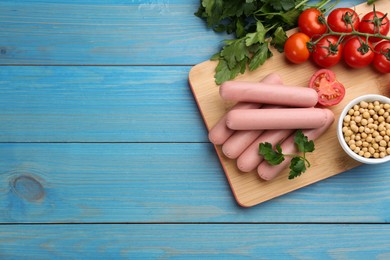 Fresh raw vegetarian sausages and vegetables on light blue wooden table, flat lay. Space for text