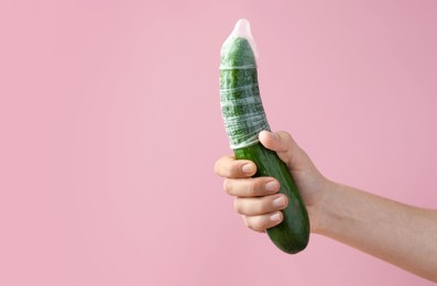 Woman holding cucumber in condom on pink background, closeup and space for text. Safe sex concept