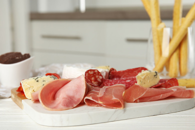 Tasty ham with other delicacies served on white wooden table, closeup