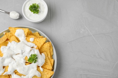 Plate of Mexican nacho chips with sauce on grey table, flat lay. Space for text