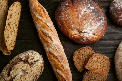 Different kinds of fresh bread on black wooden table, flat lay