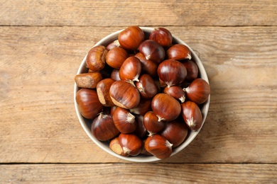 Fresh sweet edible chestnuts in bowl on wooden table, top view