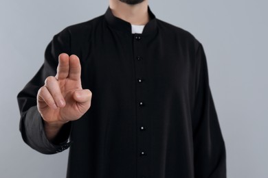 Priest making blessing gesture on grey background, closeup