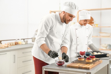 Pastry chefs preparing desserts at table in kitchen