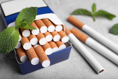Pack of menthol cigarettes and mint leaves on grey table, closeup