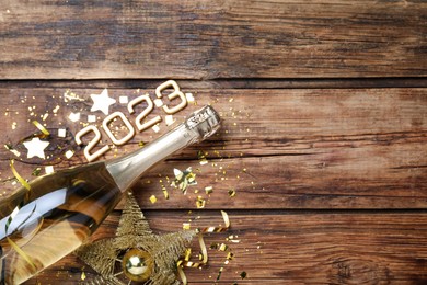 Happy New Year 2023! Flat lay composition with bottle of sparkling wine on wooden table, space for text