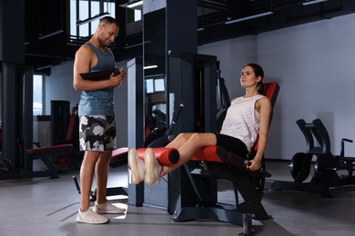 Photo of Happy trainer writing down plan of workouts while woman doing exercise in modern gym