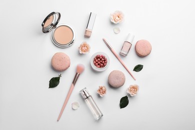 Flat lay composition with makeup products, roses and macarons on white background