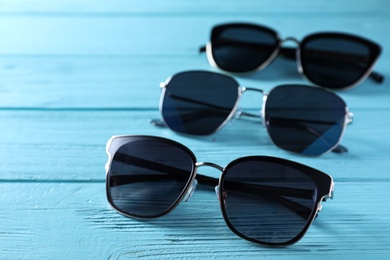Many stylish sunglasses on light blue wooden background