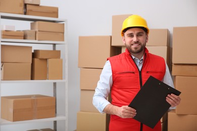 Young man with clipboard near cardboard boxes at warehouse