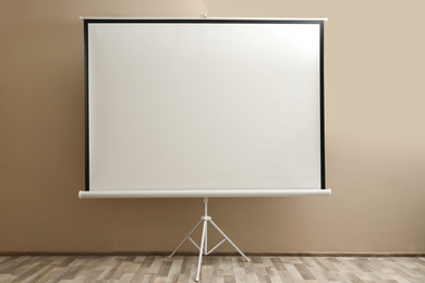 Blank projection screen near beige wall indoors. Space for design