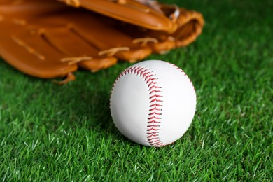 Photo of Catcher's mitt and baseball ball on green grass, closeup. Sports game