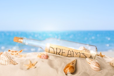 Corked glass bottle with rolled paper note and seashells on sandy beach near ocean