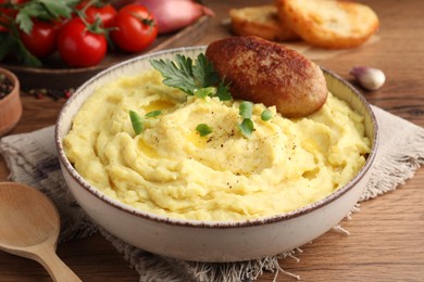 Photo of Bowl of tasty mashed potatoes with parsley, black pepper and cutlet served on wooden table, closeup