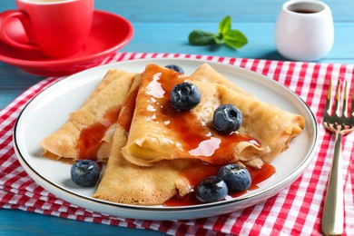 Delicious crepes served with blueberries and syrup on table, closeup